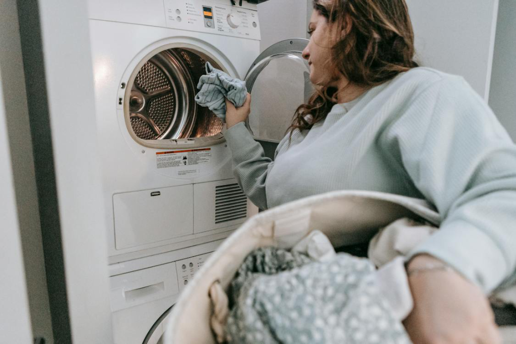 A woman holding a laundry basket and putting dirty laundry in a washing machine