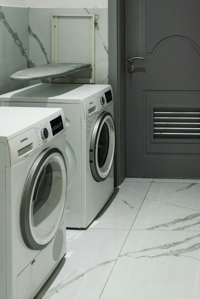  A laundry room with two washing machines and a foldable iron stand