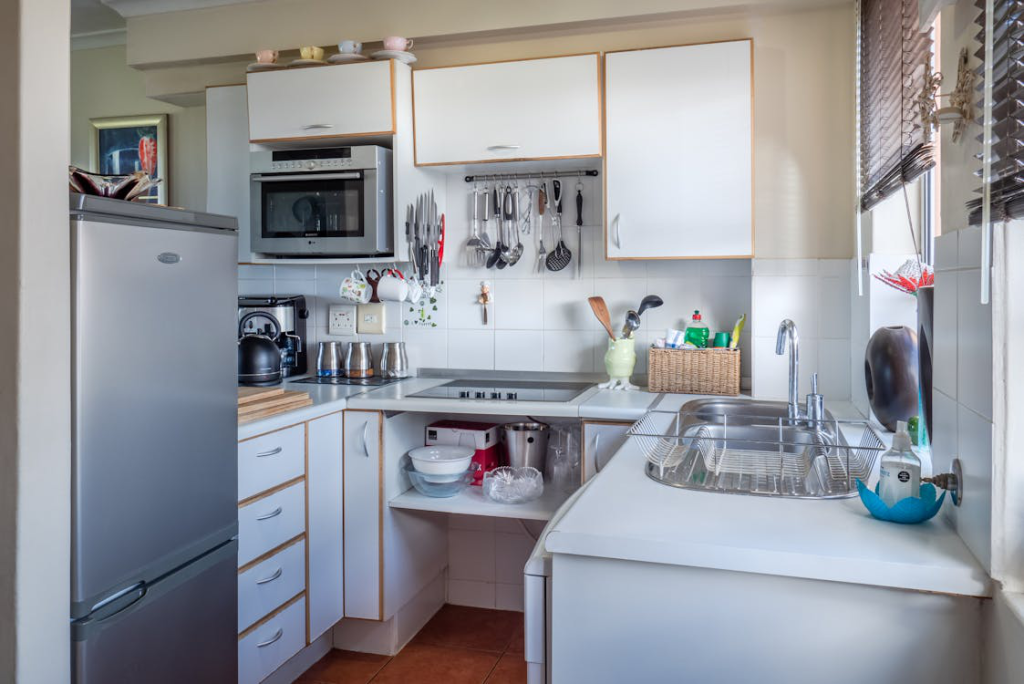 A small kitchen design with white wooden cabinets, fridge, sink, oven, etc.