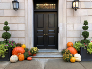 Orange pumpkins on the grey concrete floor in front of a house with a black safe entry door