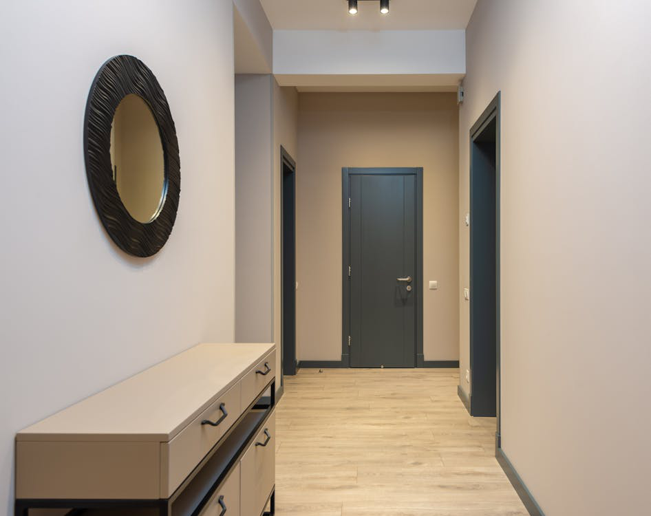 A gray colored door leading to a hallway with wooden furniture