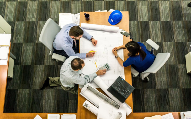 An image of people working in an office and looking over blueprints
